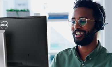 Uśmiechnięty mężczyzna w okularach korzystający z zestawu słuchawkowego i monitora Dell.